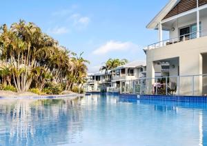 a swimming pool in front of a house with palm trees at Newly Restyled Resort 1 Bedroom Unit Oaks Pacific Blue in Salamander Bay +8 photos