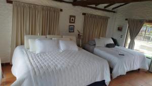 two beds in a bedroom with white sheets at Posada Iglesia Vieja in Soatá