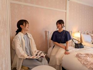 女子旅のホテル Palette STAYs パレットステイズ في Ōzu: كانتا جالستين على السرير في غرفة +5 صور