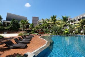a swimming pool with chaise lounge chairs next to a building at Golden Tulip Jineng Resort Bali in Kuta