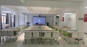 MIDI Hotel Guangdong Chaozhou Xiangqiao District Hanshan Teachers College في شاوزو: غرفة كبيرة بها طاولات وكراسي وشاشة