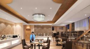 Vienna Hotel Hangzhou Jiubao Sijiqing Suanli Town في Yuhang: امرأة تقف في مطعم مع طاولات وكراسي