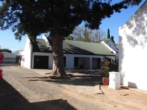 a white barn with a tree in front of it at Mountain Zebra Cottage in Graaff-Reinet