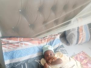 a baby laying in a crib wearing a hat at Makucha Ya Simba Homestay and camping grounds in mwanza  +6 photos