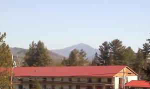a building with a red roof with mountains in the background at Carriage House Motor Inn in Lake Placid