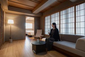 a woman sitting on a couch in a room with windows at soyo-ne kyoto sanjo in Kyoto