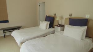 two beds in a hotel room with white sheets and blue pillows at Avocet Cottage in Knysna