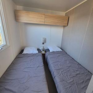 L'Oasis Mobil Home à 100m de la Plage Camping 5 étoiles في توراي: يوجد سريرين في غرفة صغيرة مع سرير إضافي