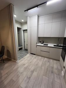 a kitchen with white cabinets and a wooden floor at Инжу Сити in Karagandy