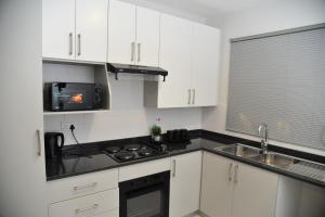 a kitchen with white cabinets and a sink and a microwave at Sentlhaga 1 Bed Self Catering Apartment, Sarona City,Habitat Kappa, Gaborone in Gaborone +8 photos