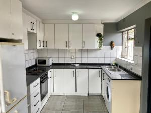 Unit 1, TraversHub Sleeps 6 Self-Catering Group Belhar, CT في Belhar: مطبخ أبيض مع دواليب بيضاء ومغسلة