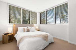 ein weißes Schlafzimmer mit einem Bett und Fenstern in der Unterkunft Upper North Shore Haven - A Tranquil Treetop Escape in Warrawee