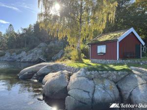 a red cabin on the side of a river with rocks at Dog-friendly cottage with boat & private jetty at Tjörn SE09170 in Krommeröd