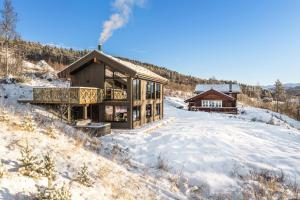 Una cabaña de madera en la nieve con terraza en New luxury cabin in Geilo with hot tub, mountain views & ski access, en Lii