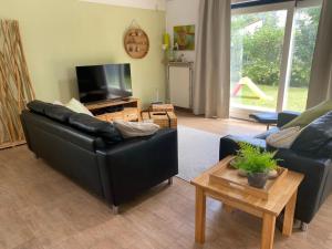 a living room with a black leather couch and a television at Villa Noordenwind in Julianadorp