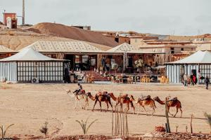 Agafay Yes We Camp Restaurant & Spa في Aït Mazou: مجموعة من الأشخاص يركبون الجمال أمام مبنى