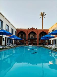a large swimming pool with chairs and blue umbrellas at Dahab Now in Dahab