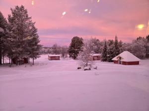 a snow covered field with houses and trees with a sunset at Kaamasen Kievari in Kaamanen