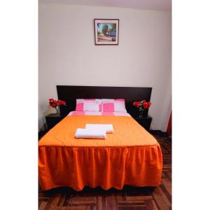 a bedroom with a bed with orange sheets and pink pillows at Hostal Bless Tacna in Tacna