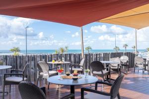 a patio with tables and chairs and the ocean at Hôtel de la Baie - Thalassothérapie PREVITHAL in Donville-les-Bains