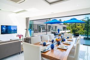 Peaceful 4Br Luxury Villa Elena Walk to Beach في Ban Hua Laem Ma So: غرفة طعام بها طاولة خشبية ومظلات زرقاء