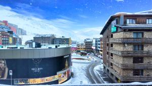 een met sneeuw bedekte stad met gebouwen en een berg bij Hotel Catanies in Pas de la Casa