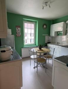 Appartement La Vanne Confortable et équipé في لابريس: مطبخ بجدران خضراء وطاولة وكراسي