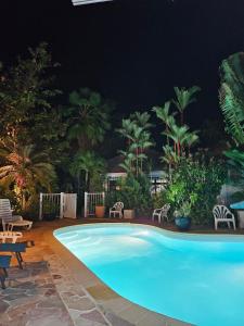 una piscina por la noche con sillas y palmeras en Villa Patio Colibri, en Chambort