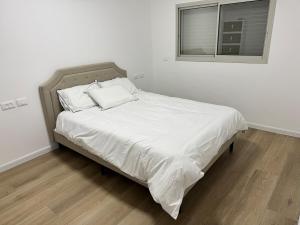 Una cama con sábanas blancas y una ventana en una habitación en Bimat HaTzafon, en Kiryat Shemona