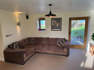 a living room with a brown couch and a window at Woodland Forge - The Stables in Over Whitacre