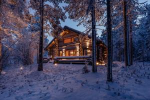 a log cabin in the woods in the snow at night at Kelokurki - The Luxury Lodge Where Serenity Meets the Northern Lights in Levi