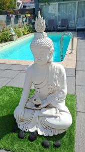 Eine weiße Statue sitzt auf dem Rasen neben einem Pool. in der Unterkunft Budha GuestHouse in Porto