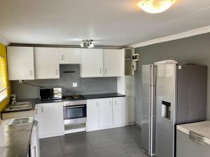 Unit 2 TraversHub Sleeps 6 Self-Catering Group Belhar, CT في Belhar: مطبخ بخزائن بيضاء وثلاجة من الفولاذ المقاوم للصدأ
