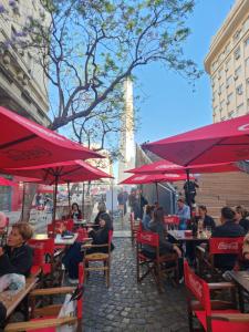 Obelisco Buenos Aires في بوينس آيرس: مجموعة من الناس يجلسون على الطاولات مع المظلات الحمراء
