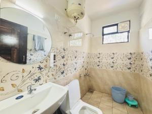 Un baño con lavabo, inodoro y espejo. en Aroha home stay, en Pālampur
