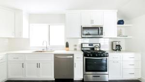 a white kitchen with a stove and a microwave at ONeill I by AvantStay Coastal Paradise Steps from Beach Modern Decor in Newport Beach +8 photos