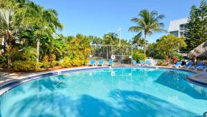 a large swimming pool with blue chairs and palm trees at Dune Wind South by AvantStay Communal Pool Hot Tub Gated Community Close to Smathers Beach Month Long Stays Only in Key West