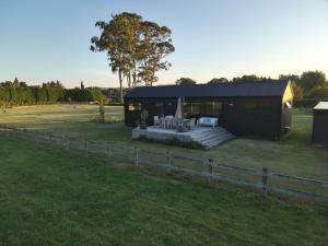 a small black building with a fence next to a field at Kotuku Cottage in Tauranga