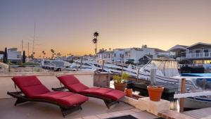 two red chairs sitting on a patio next to a boat at Canalfront Charmer by AvantStay Waterfront w Shared Dock Hot Tub in Newport Beach