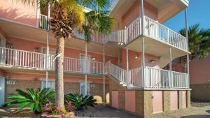 a pink building with a palm tree in front of it at Beachfront Condo Prvt Balcony w View Pool Access Beach Happy by AvantStay in Port Aransas