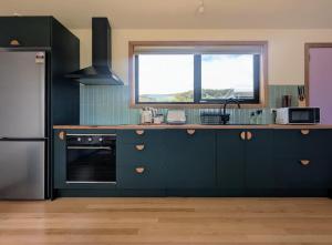 Sisters Beach Hideaway - A Coastal Escape في Sisters Beach: مطبخ مع دواليب زرقاء داكنة ونافذة