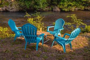 trois chaises bleues et une table au bord d'une rivière dans l'établissement Roaring River Resort, à Roaring Creek