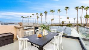Velvet Sand I by AvantStay Steps to Newport Beach Private Rooftop w Outdoor Kitchen Hot Tub في شاطئ نيوبورت: طاولة على شرفة مع شواية وأشجار نخيل