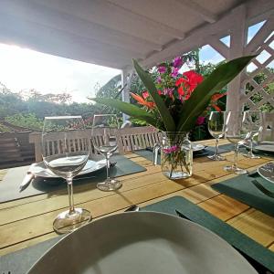Villa Fleurs d'Air en côte sous le vent في ديساي: طاولة خشبية مع كؤوس للنبيذ و إناء من الزهور +30 صورة