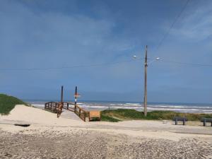 a sandy beach with a wooden walkway to the ocean at duplex aconchegante in Tramandaí