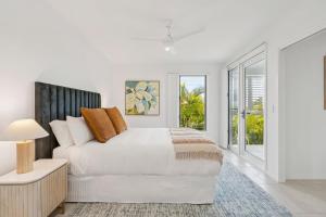 a white bedroom with a large bed and windows at The Cheeky Palm - Beachy, enjoy a cheeky cocktail! in Woolgoolga