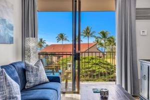 a living room with a blue couch and a balcony with palm trees at Hip Oceanfront Resort Vistas in Kihei