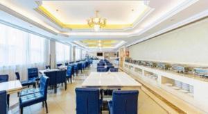 Vienna Classic Hotel Qingdao Huangdao في هوانغادو: غرفة طعام بها كراسي وطاولات زرقاء وثريا