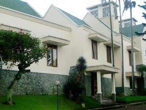 a white house with a stone wall and a tree at Bumi Ciherang Hotel in Puncak