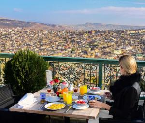 a woman sitting at a table with a view of a city at Palais Faraj Suites & Spa in F&egrave;s